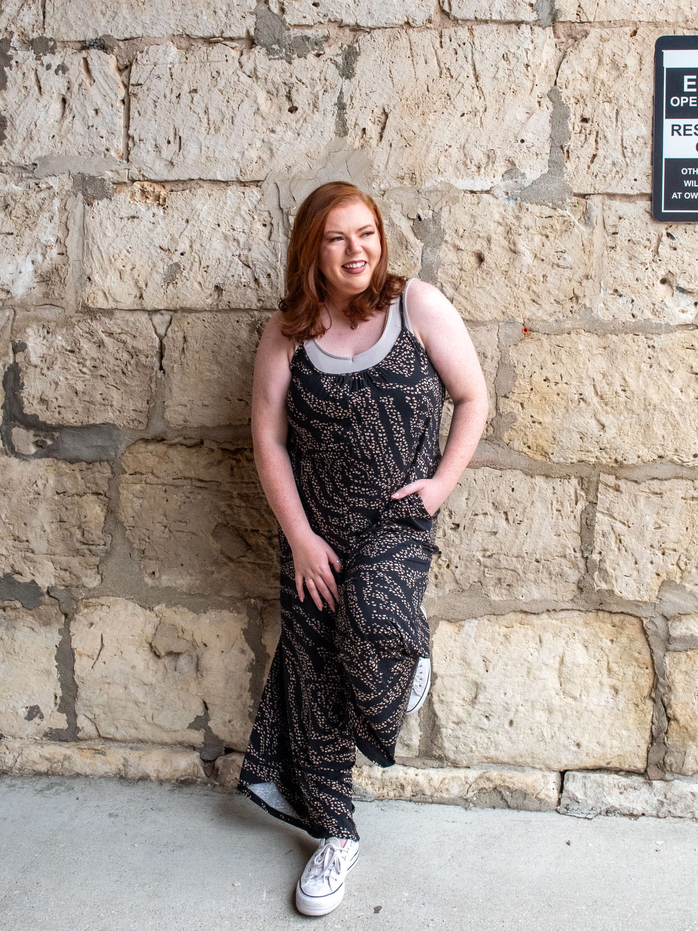 A model wearing a flared leg, black, animal print jumpsuit. She has it layered over a light gray tank top and white sneakers.
