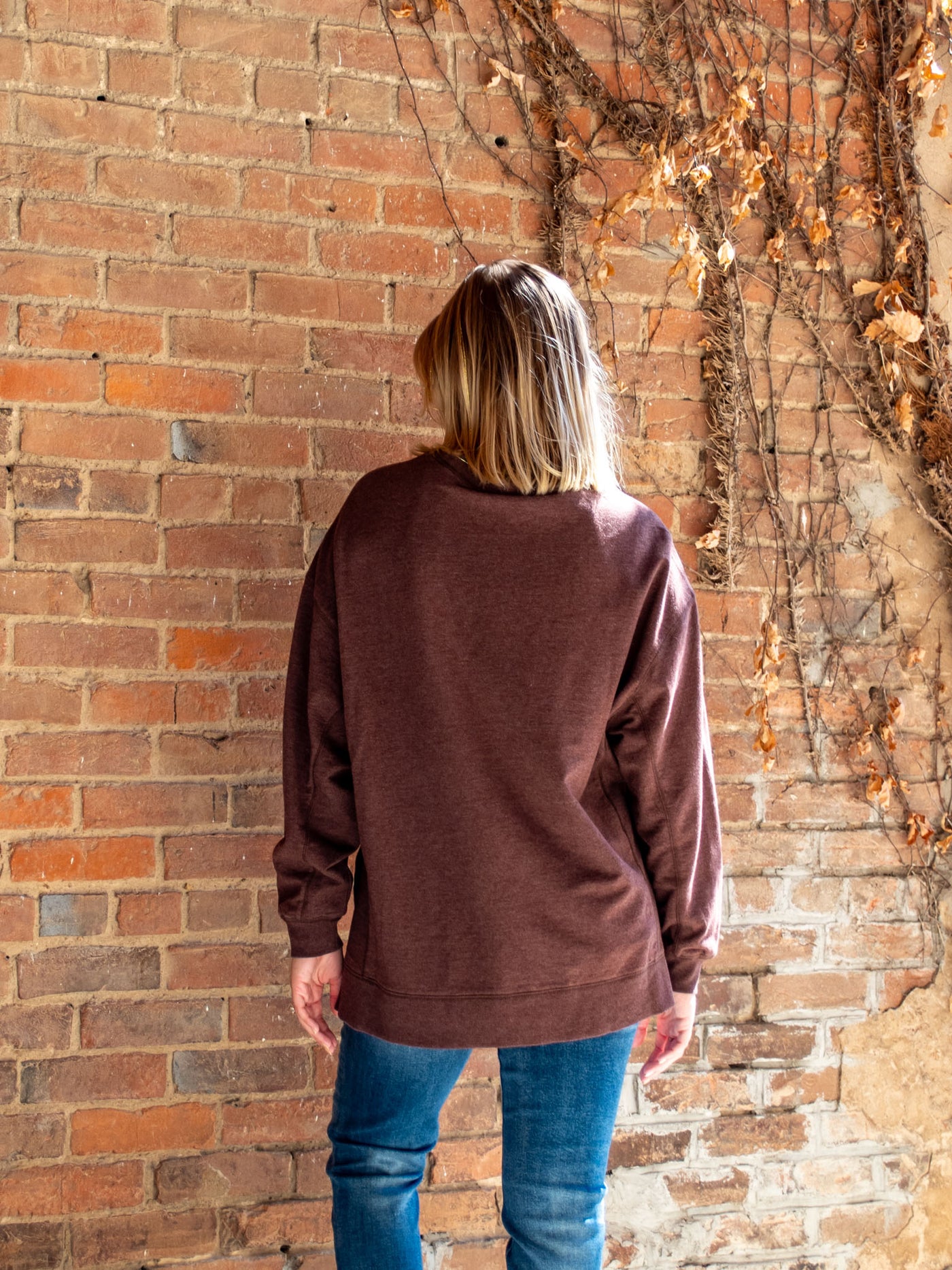 A model wearing a maroon crewneck sweatshirt. The model has it paired with a medium wash skinny jean.