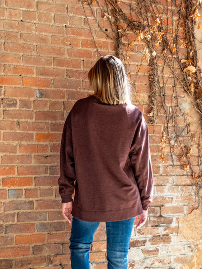 A model wearing a maroon crewneck sweatshirt. The model has it paired with a medium wash skinny jean.