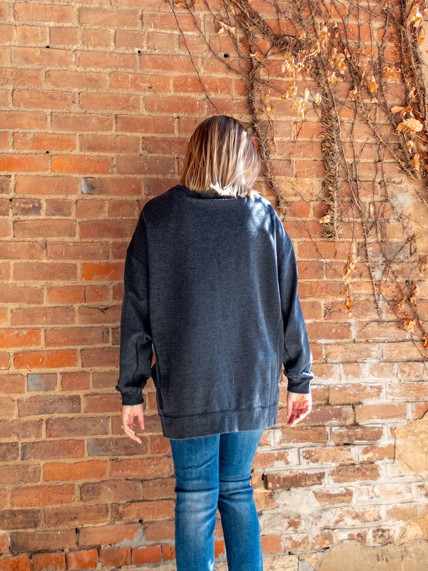 A model wearing a charcoal crewneck sweatshirt. The model has it paired with a medium wash skinny jean.