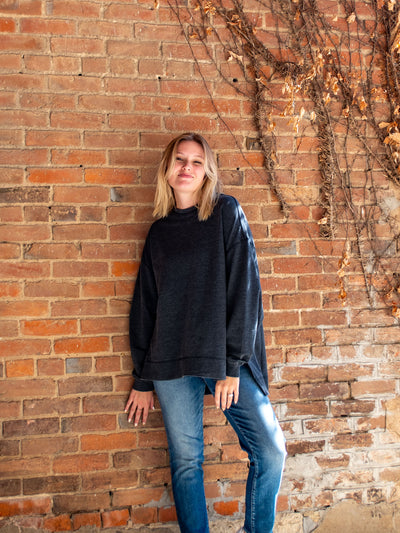 A model wearing a charcoal crewneck sweatshirt. The model has it paired with a medium wash skinny jean.