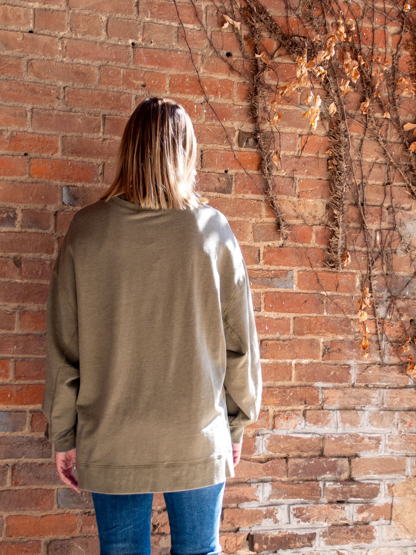 A model wearing a olive crewneck sweatshirt. The model has it paired with a medium wash skinny jean.