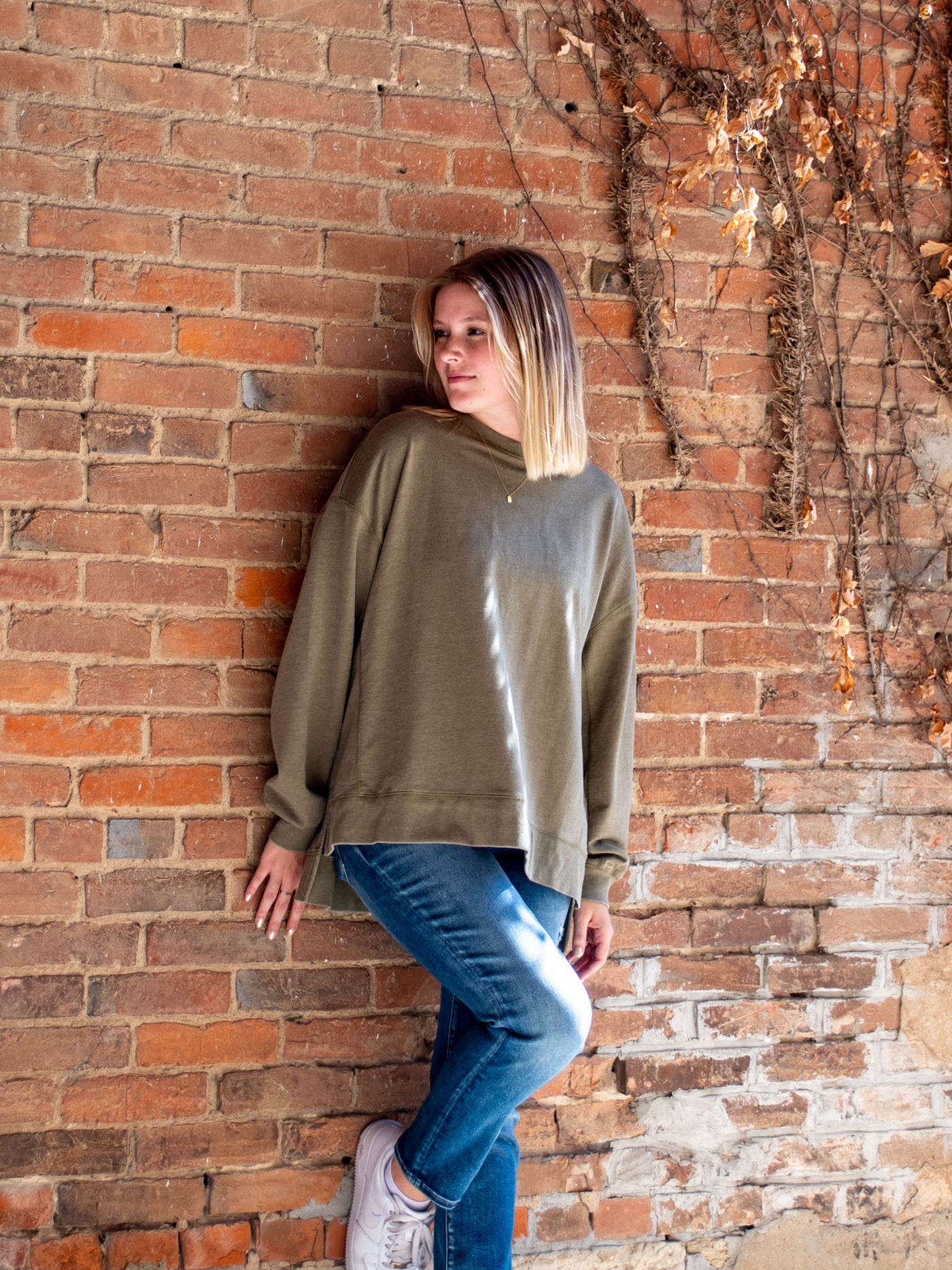 A model wearing a olive crewneck sweatshirt. The model has it paired with a medium wash skinny jean.