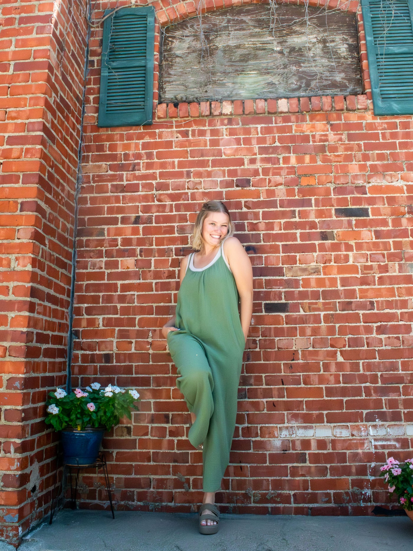 A model wearing an olive green, gauze jumpsuit. The model paired it with a beige tank underneath and beige platform sandals.