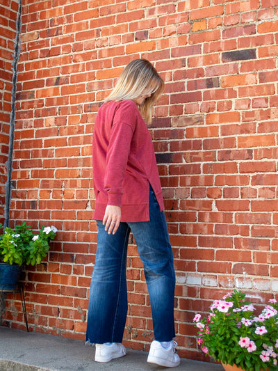A model wearing a red v-neck oversized sweatshirt. The model has it paired with a dark wash, wide leg jean and white sneakers.