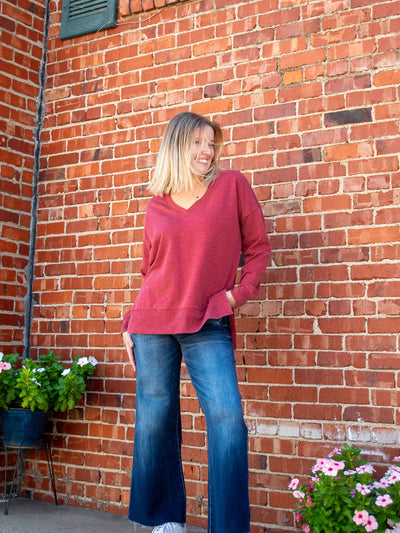 A model wearing a red v-neck oversized sweatshirt. The model has it paired with a dark wash, wide leg jean and white sneakers.