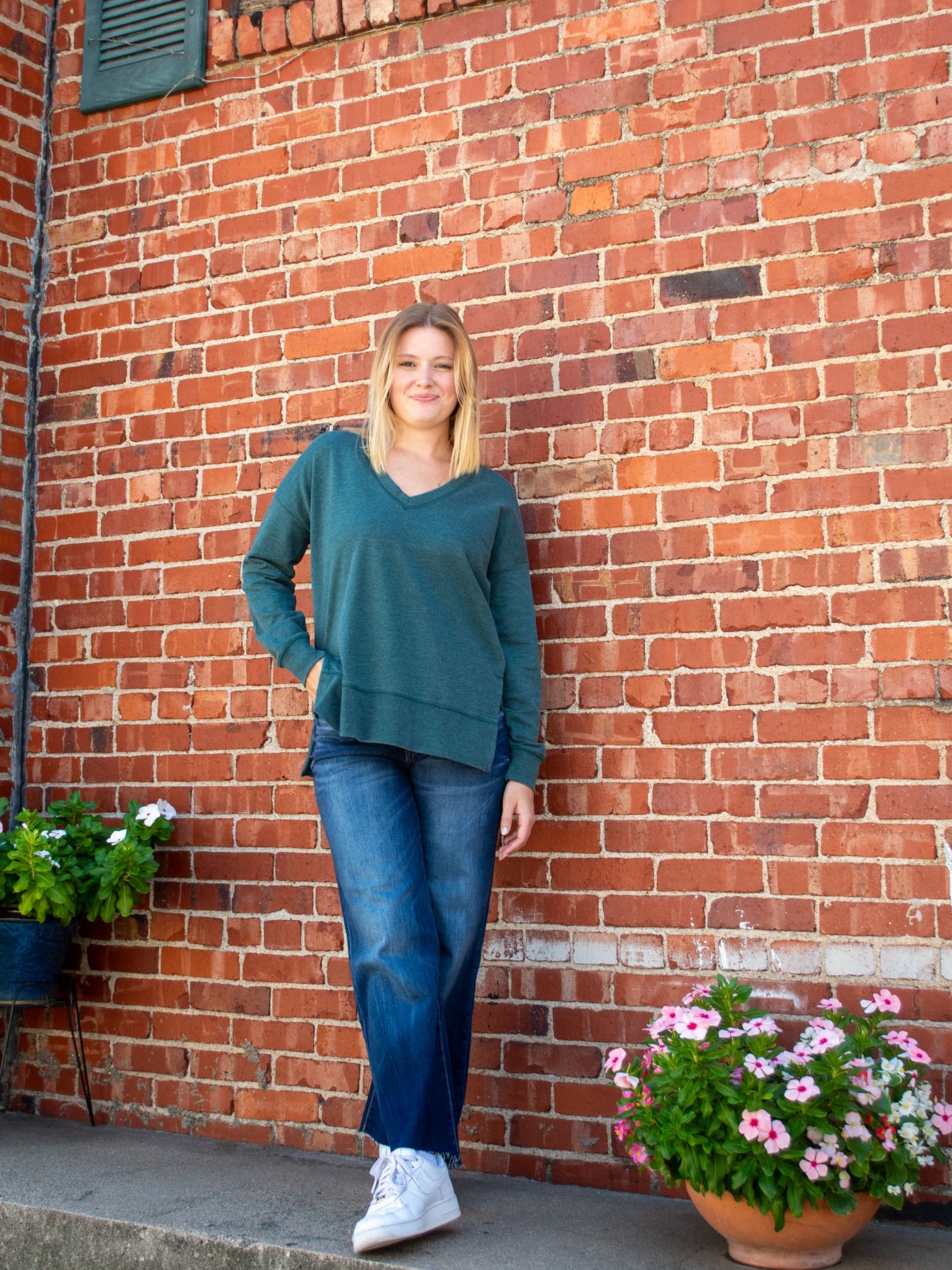 A model wearing a teal v-neck oversized sweatshirt. The model has it paired with a dark wash, wide leg jean and white sneakers.
