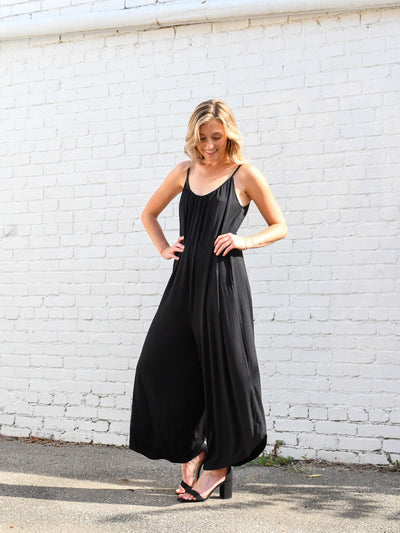 A model wearing a spaghetti strap black flared jumpsuit. The model is wearing it with black high heels.