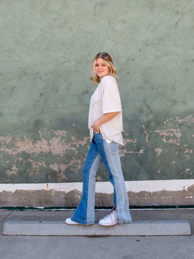 A model wearing a pair of high rise flare side inset jeans with a hem slit. She has it on with an oversized relaxed cream tee with white sneakers.