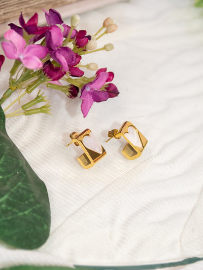 A pair of gold studs with a white pearlescent heart set in them.