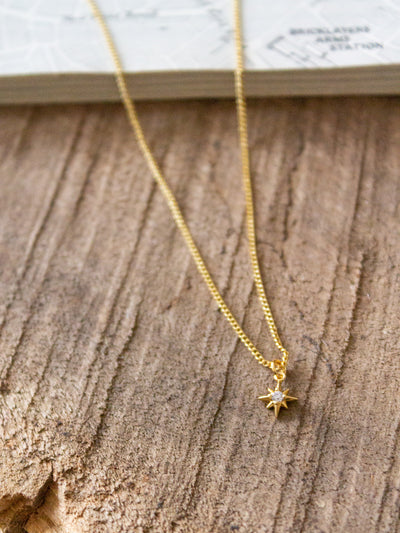 A gold chain necklace with a small star charm with a cubic crystal.