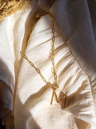A square link/ paperclip style chain necklace with a twisted capital M attached to it.