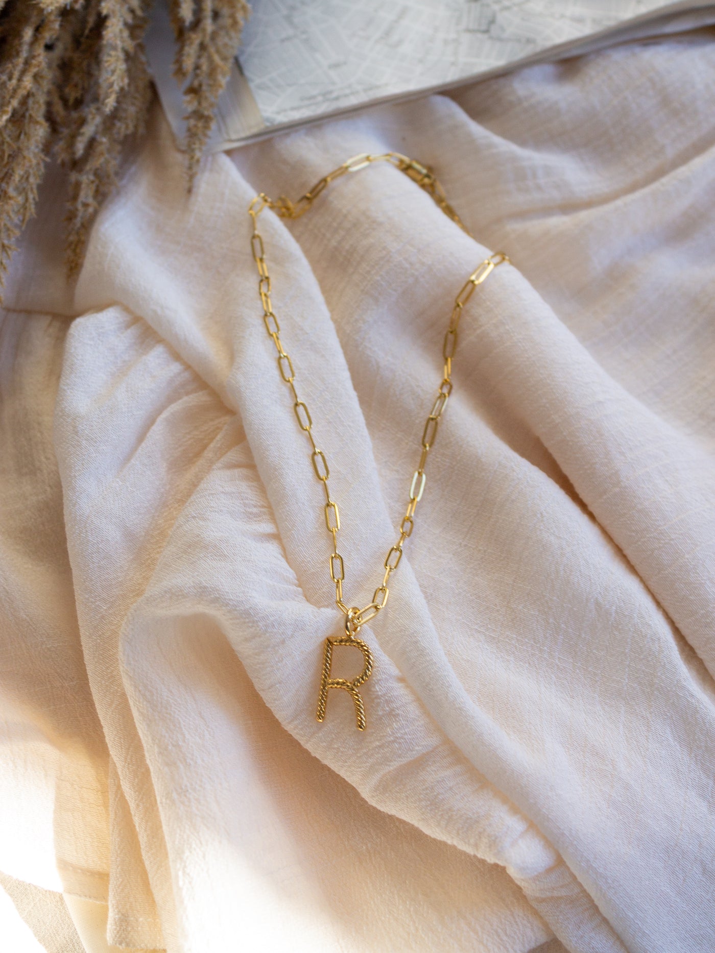 A square link/ paperclip style chain necklace with a twisted capital R attached to it.