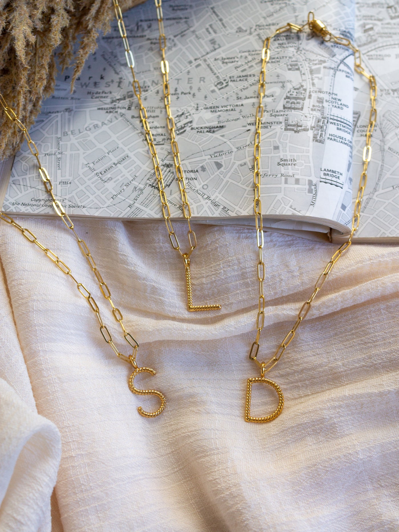 A group of square link chain necklace with with a twisted gold initial attached. The letters are S, L, and D.