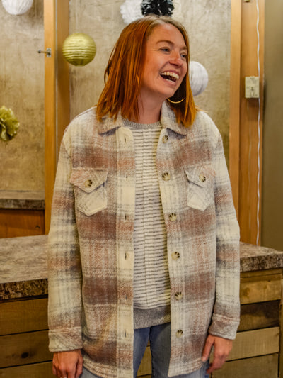 A model wearing a plaid shacket over a grey and white sweater with jeans.