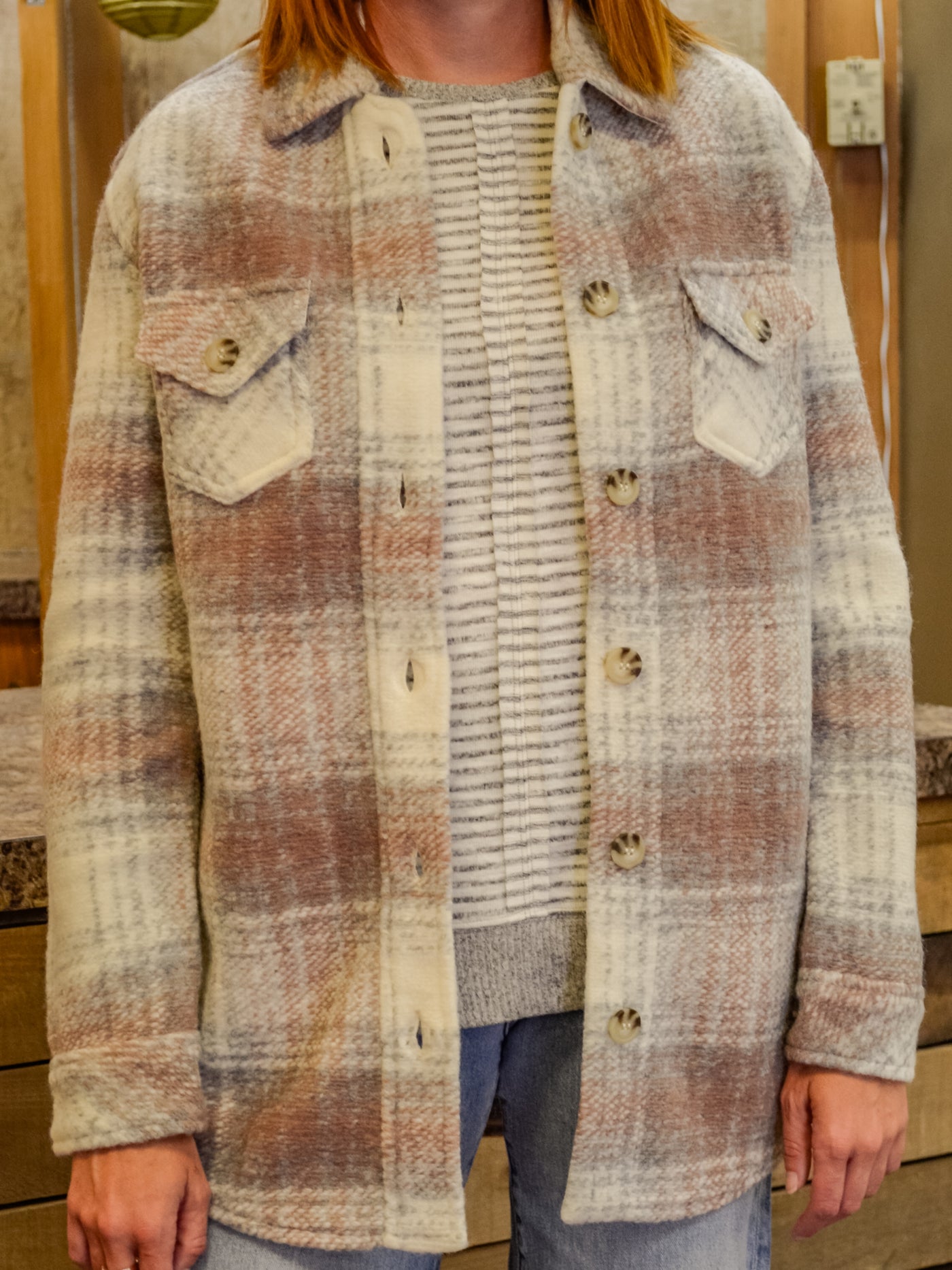 A model wearing a plaid shacket over a grey and white sweater with jeans.