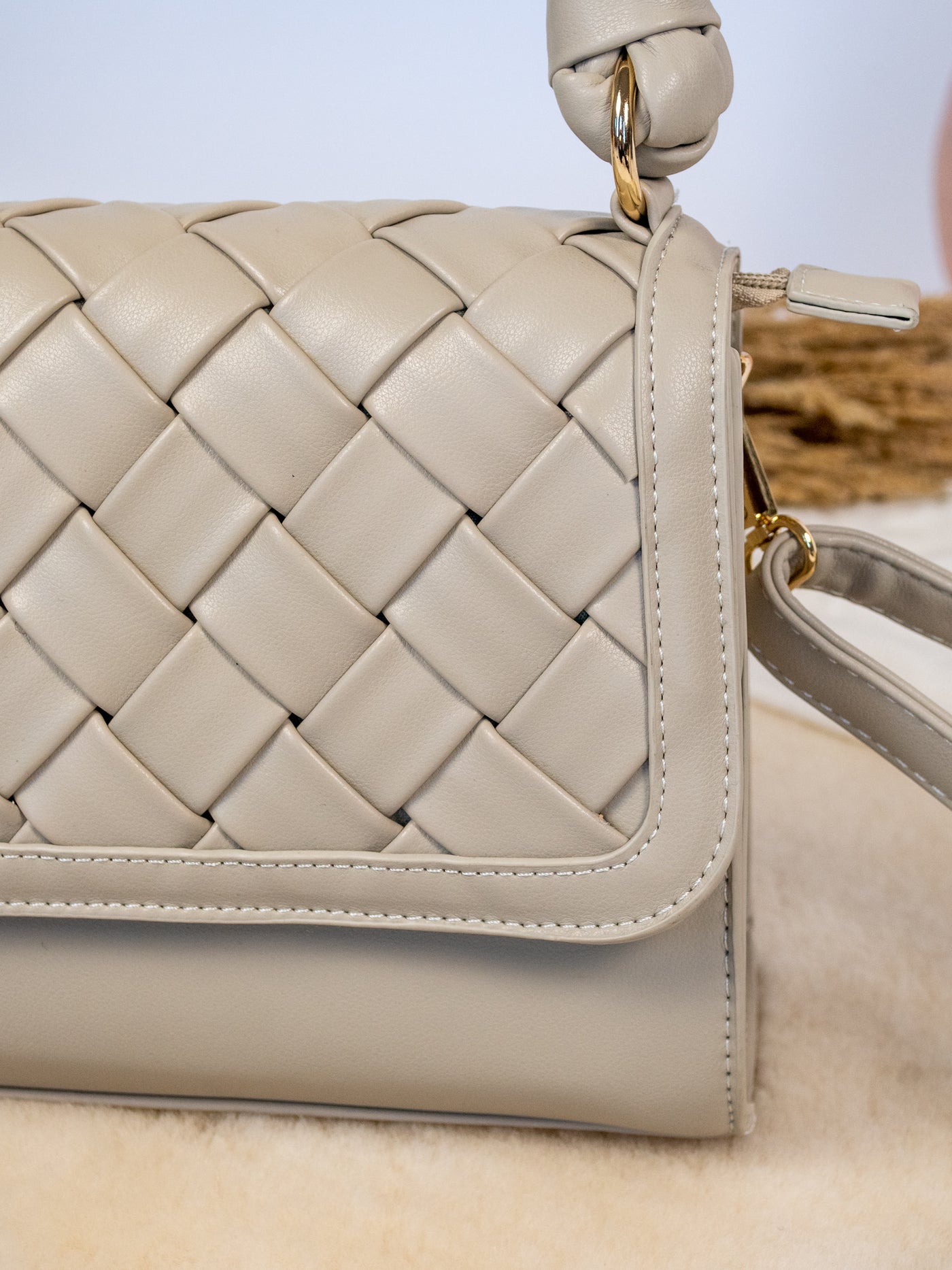 A cream colored purse with an adjustable strap and woven look. It has a braided top handle is cream colored.