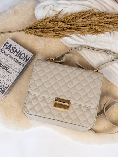 A cream colored quilted backpack with gold hardware.