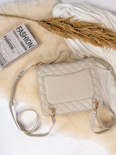 A cream colored quilted backpack with gold hardware.