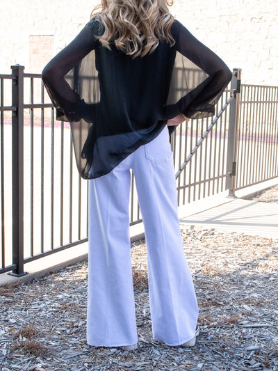 A model wearing a pair of white high rise wide leg denim with a black silk kaftan blouse.
