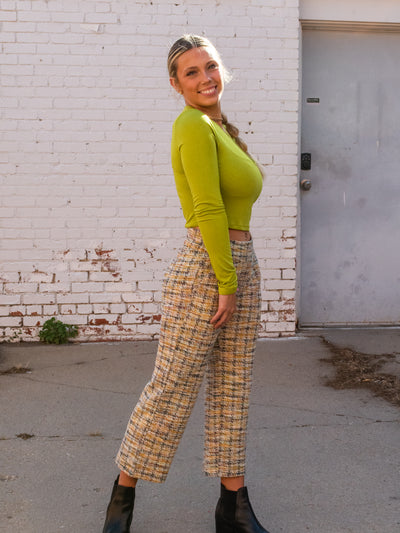 A model wearing a green long sleeve crop top with a cutout. She has it on with plaid boucle pants and black booties.
