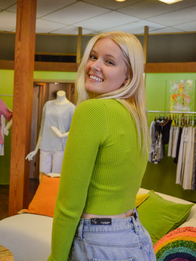 A model wearing a long sleeve cropped ribbed sweater with an oval cutout on the front. She has it paired with a lightweight denim mini skirt.