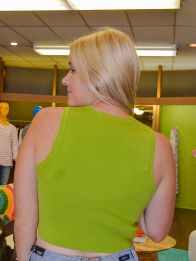 A model wearing a lime green cropped sweater tank/ Sweater vest. She has it styled with a denim skirt.