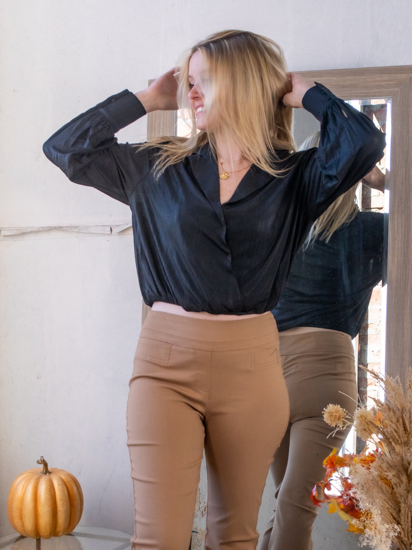 A model wearing a black crossover blouse with a cropped fit. She has it paired with tan pants.