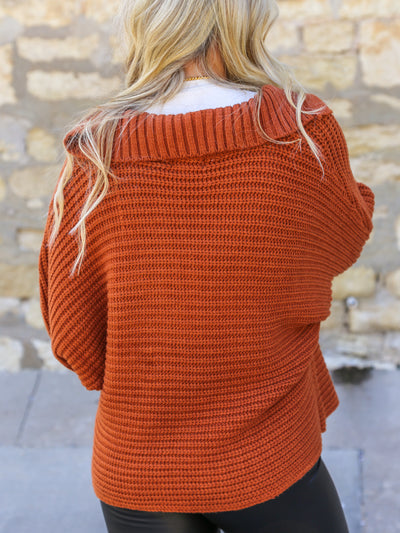 A model wearing a burnt orange v-neck sweater with black pleather leggings.
