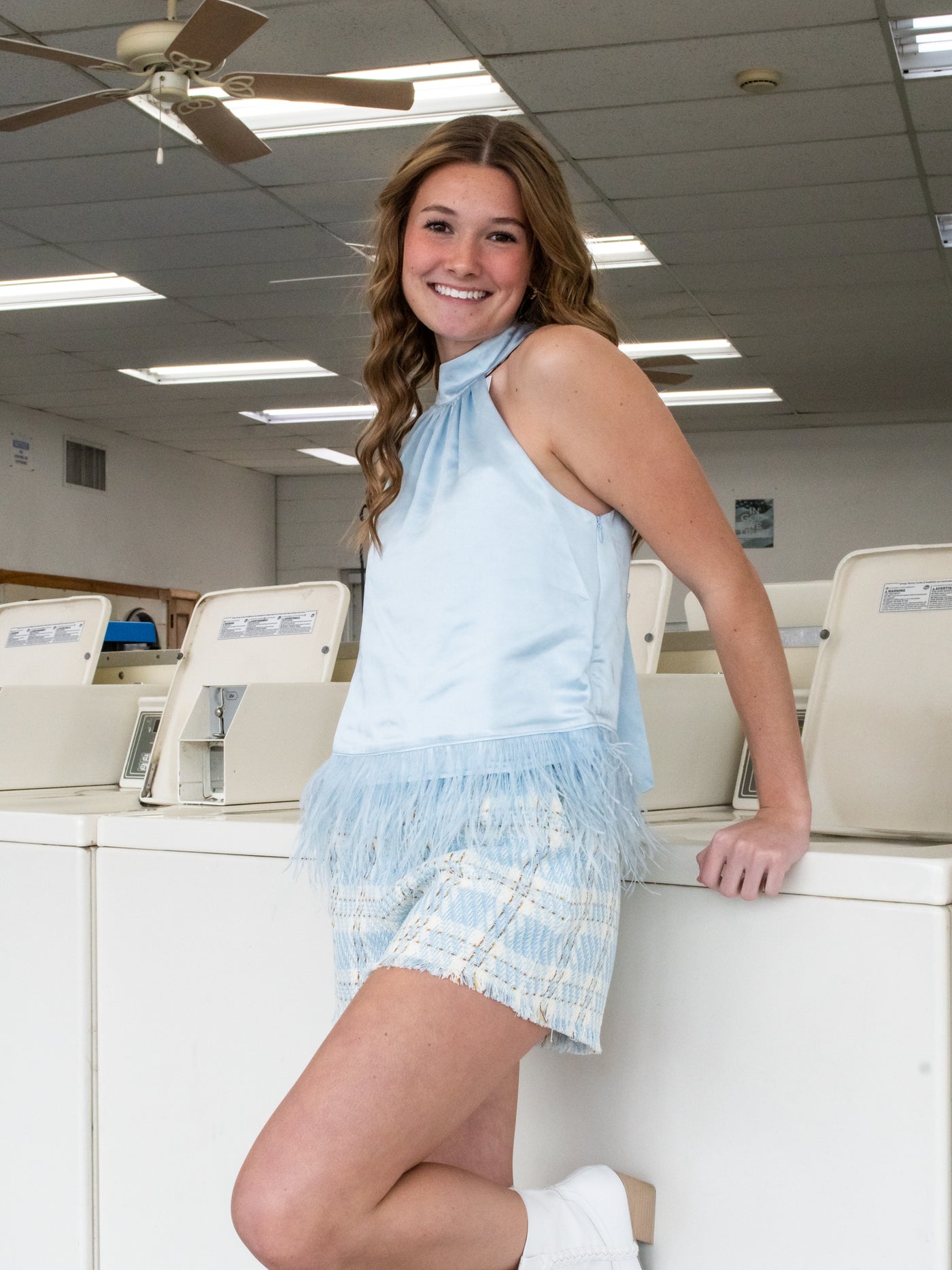 A blue halter silhouette satin shirt with feather trim. The model has it on with blue plaid shorts.