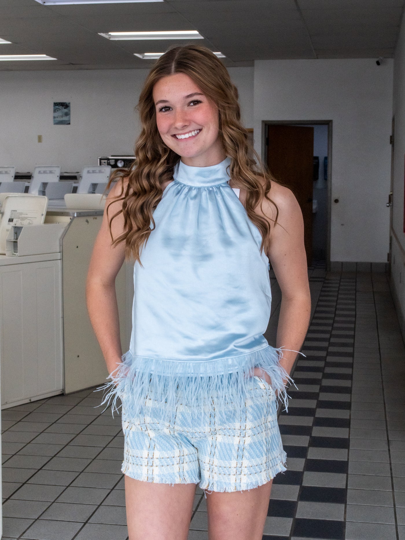 A blue halter silhouette satin shirt with feather trim. The model has it on with blue plaid shorts.