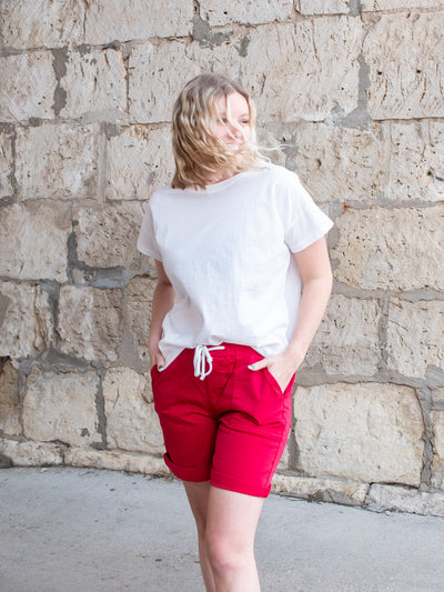 A model wearing a pair of red Bermuda sailor shorts with a white tee and white sneakers.