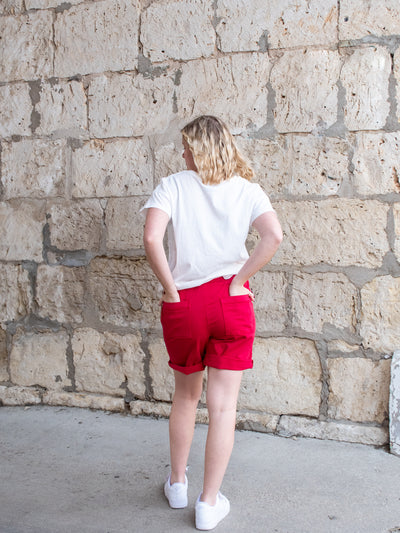 A model wearing a pair of red Bermuda sailor shorts with a white tee and white sneakers.
