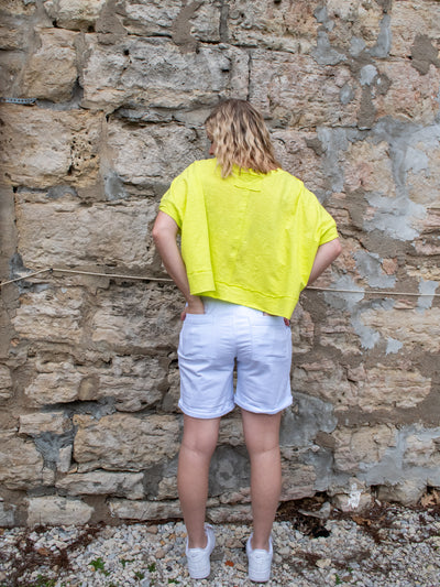 A model wearing a lime colored boxy tee with white Bermuda sailor shorts with white sneakers.