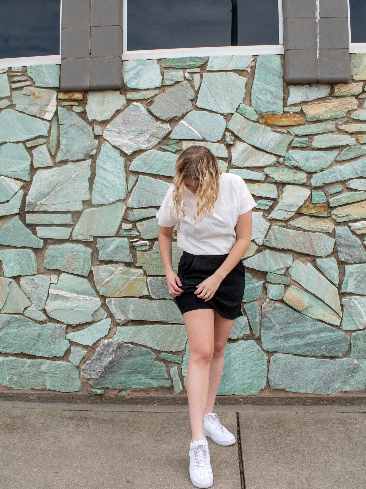 A model wearing a black crinkle material mini skort with with a white short sleeve crewneck tee and white sneakers.