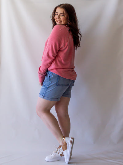 A model wearing a pair of light wash, drawstring waist shorts with a pink sweatshirt. The model has it on with a pair of white sneakers.