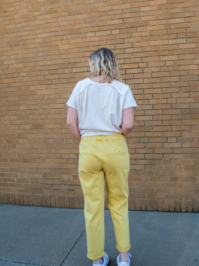 A model wearing a pair of mustard yellow drawstring pants with a white tee and white sneakers.