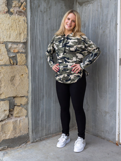 A model wearing a black Ponte knit pant/legging with a camo hoodie and white sneakers. 