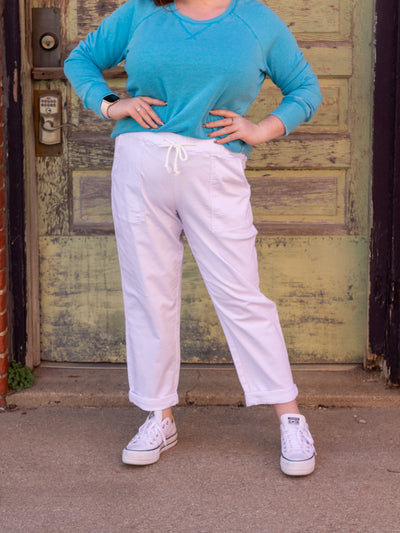 A model wearing a pair of white denim drawstring jeans with big rectangular pockets. The model has it paired with white sneakers and an aqua blue sweatshirt.