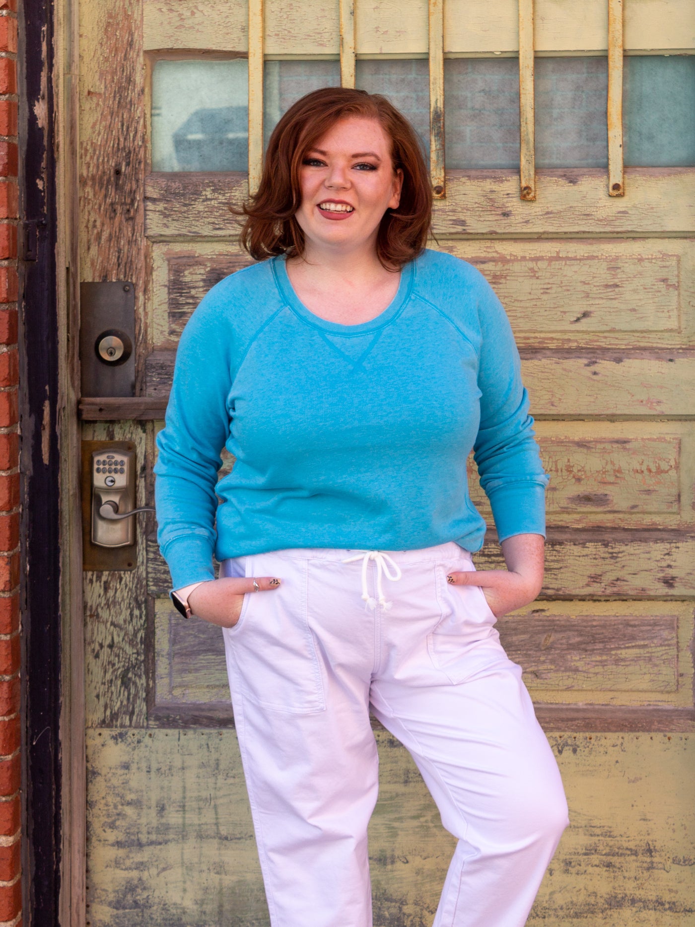 A model wearing a pair of white denim drawstring jeans with big rectangular pockets. The model has it paired with white sneakers and an aqua blue sweatshirt.