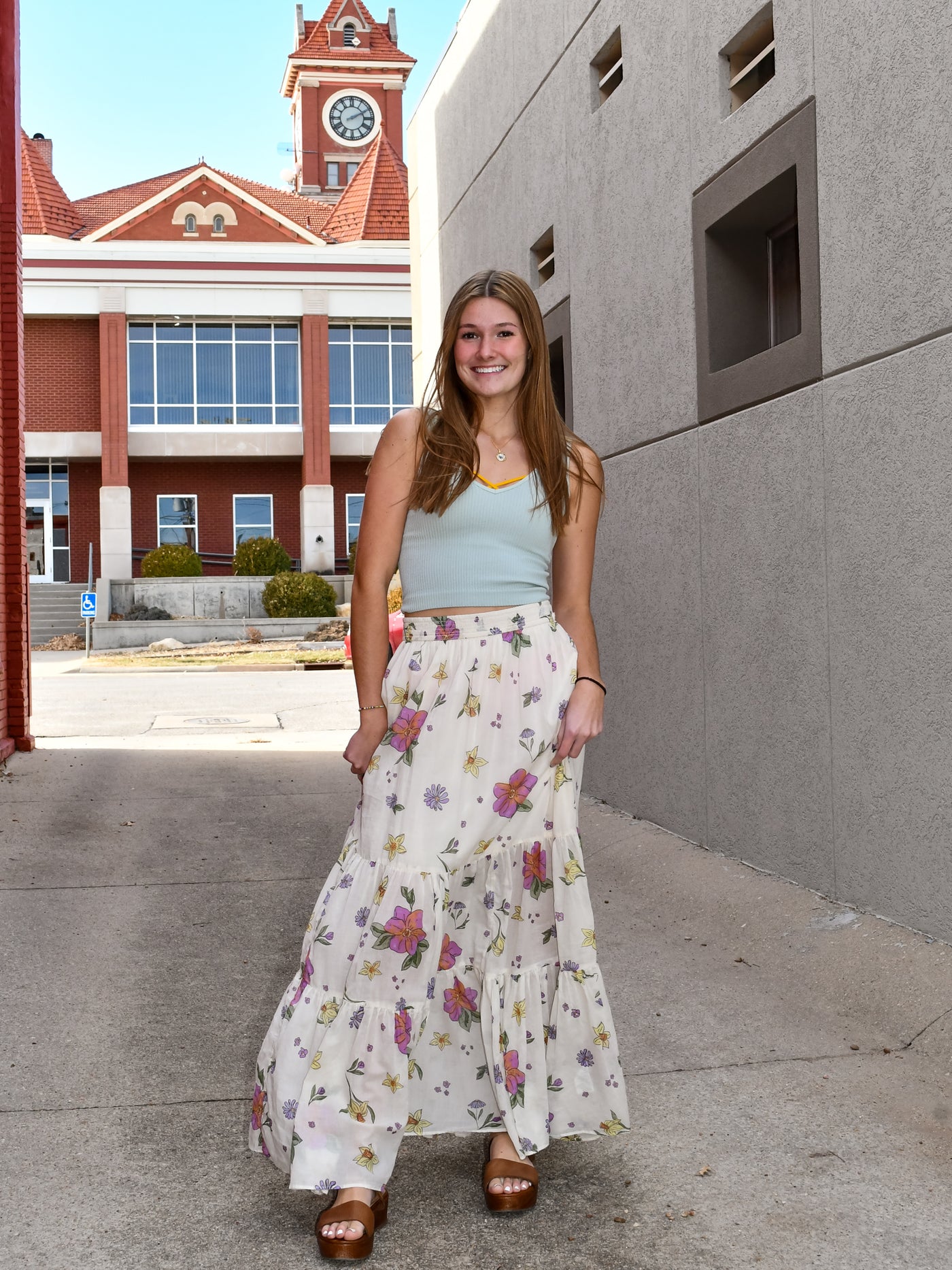 A model wearing a blue v-neck seamless tank with a floral maxi skirt and brown sandals.