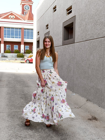 A model wearing a cream maxi skirt/dress with an allover floral print. The model has it paired with a blue seamless tank and brown sandals.