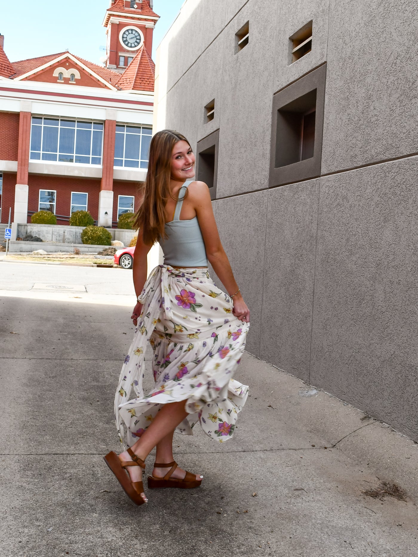 A model wearing a cream maxi skirt/dress with an allover floral print. The model has it paired with a blue seamless tank and brown sandals.