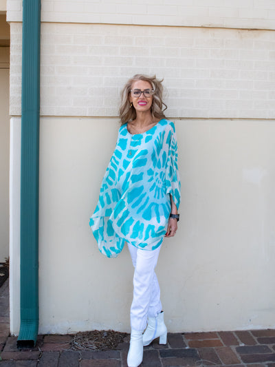 A model wearing a turquoise and white tie dye silk 3/4 length sleeve Kaftan with white denim and sandals. 