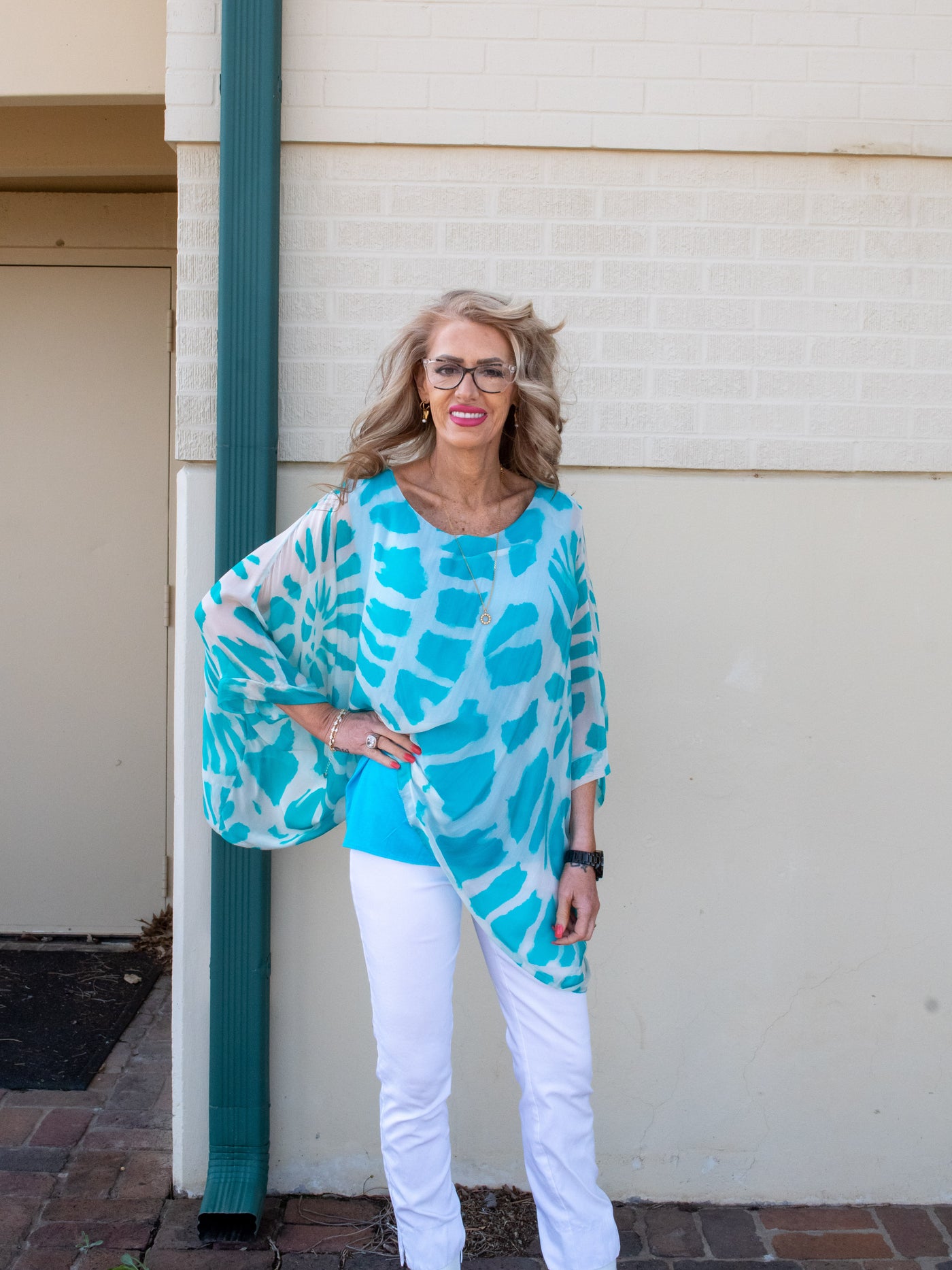 A model wearing a turquoise and white tie dye silk 3/4 length sleeve Kaftan with white denim and sandals. 