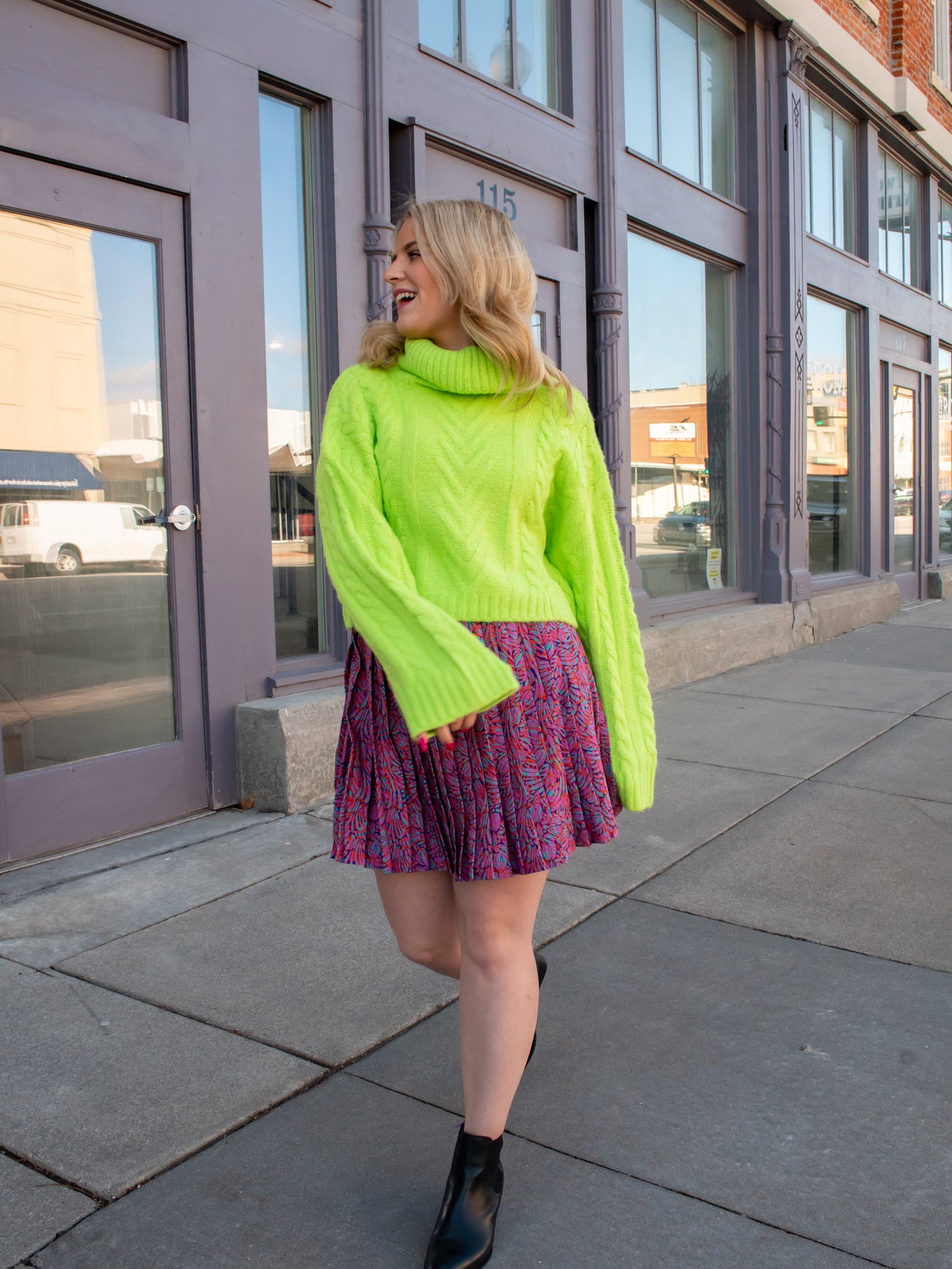 A model wearing a purple printed pleated skirt with a lime green sweater.