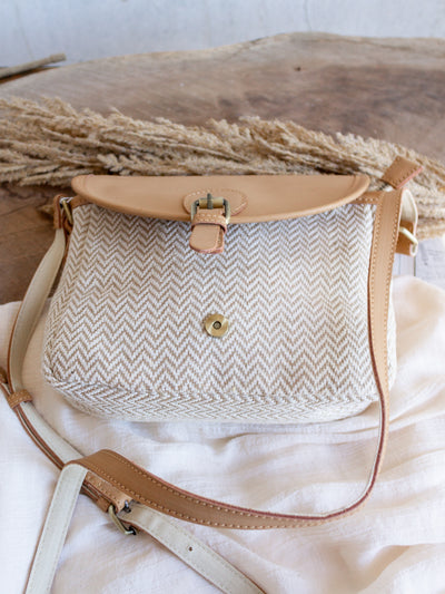 A herringbone pattern bag in cream and taupe. The bag has vegan leather accents with a pantina style flapper. 