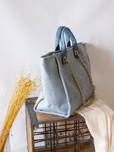 A blue fabric tote with a fabric and gold hardware chain strap.