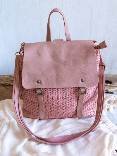 A pink woven backpack with a leather flap, leather tote strap, leather shoulder strap. It snaps close.