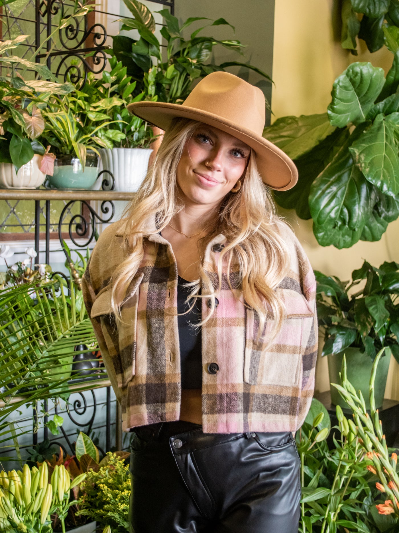 A model wearing a tan wide brim hat with a leopard band around it. She has it on with a plaid shacket and pleather pants.
